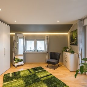 Modernes Schlafzimmer mit großem weißen Kleiderschrank, grüner Teppich und Zimmerpflanzen.