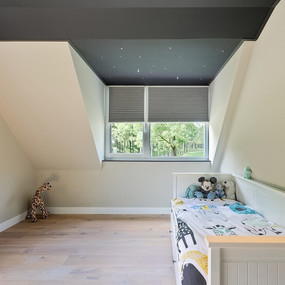 Modernes Kinderzimmer mit Dachschräge, Holzboden, Kinderbett und Stofftieren am Fenster.